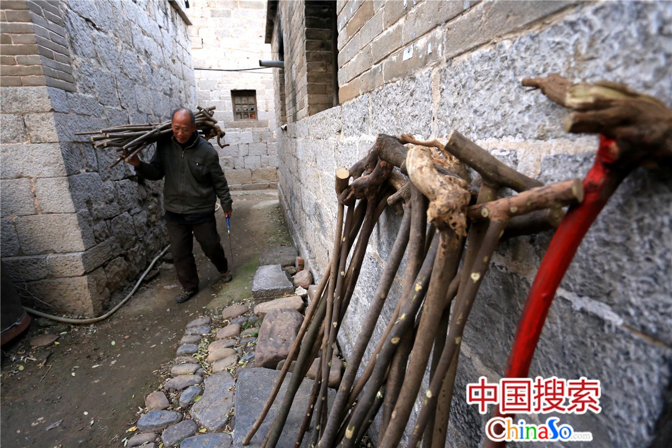 为2018年11月24日，河南鹤壁，张斗贵将从山上捡回的枯木扛回家加工成登山拐杖。